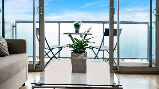 A balcony with a glass table, a potted plant, and a view of the sea.