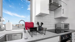 A modern kitchen with a stainless steel sink, a red appliance, a microwave, and a view of the city.
