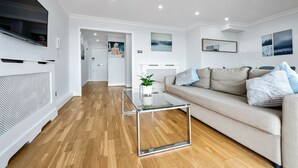 A modern living room with a beige sofa, a glass coffee table, and wooden flooring.