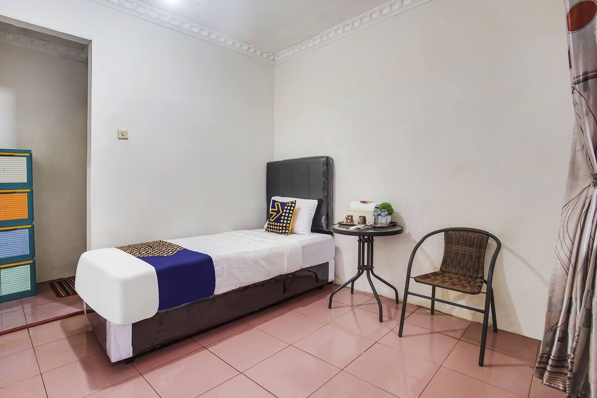 Une petite pièce, bien rangée, avec un lit simple, une petite table, une chaise et une bibliothèque.