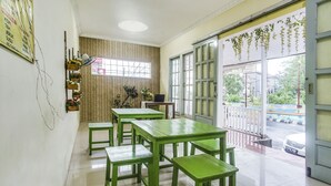 Een kamer met groene tafels en bankjes, een raam met gordijnen en uitzicht op buiten.