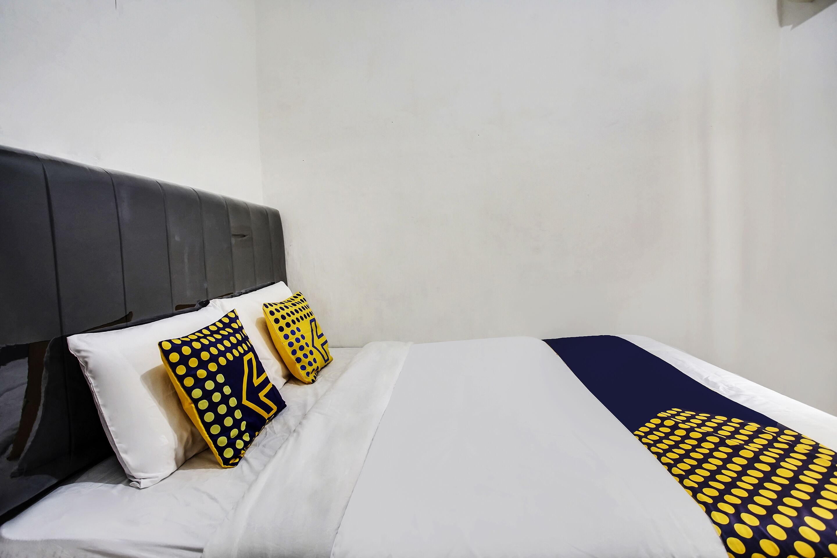 A neatly made bed with white and navy bedding, two pillows with yellow and navy patterns, and a dark headboard.