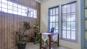 Een kamer met een houten tafel, twee planten in potten, een laptop en een raam met uitzicht op groen.