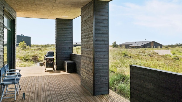 Une terrasse extérieure dotée d’un barbecue et de chaises, entourée d’un paysage naturel et bordée d’une architecture moderne.