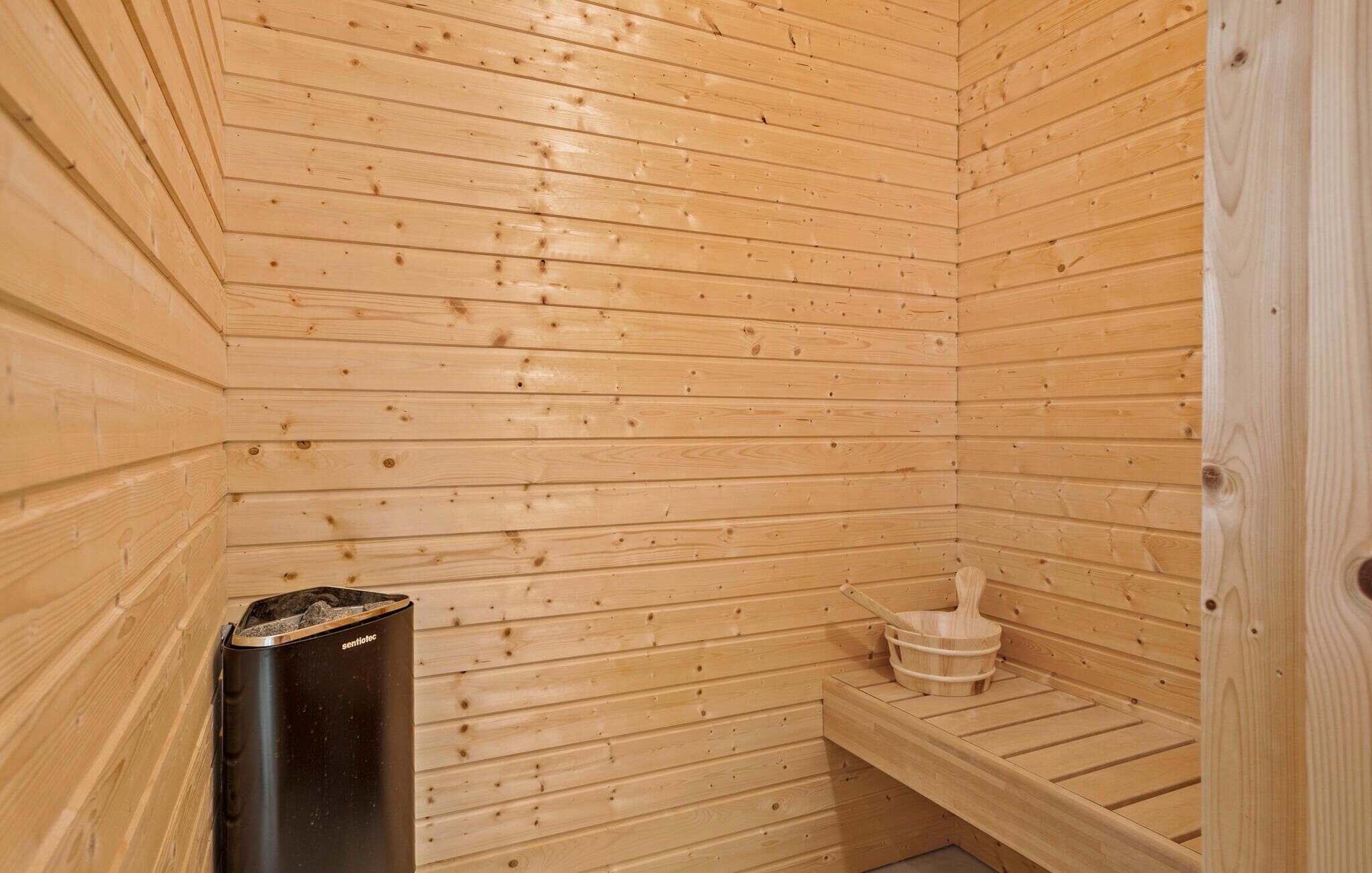 Un sauna en bois, avec un banc, un appareil de chauffage noir et un seau en bois.