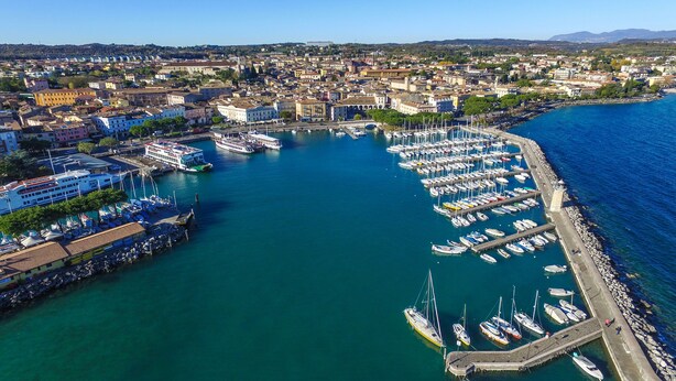 An aerial view of a marina with numerous boats docked, a large cruise ship, and a cityscape in the background. - Domus Raffaella (Arco)