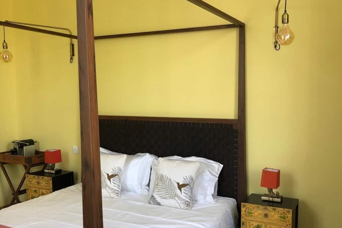 A four-poster bed with white linens and decorative pillows, a wooden headboard, and two bedside tables with red lamps.