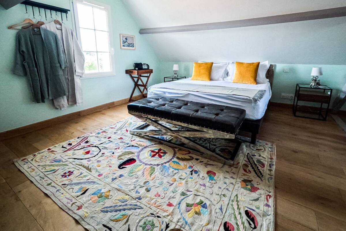 A bedroom with a bed, a colorful rug, a wooden floor, and a window.