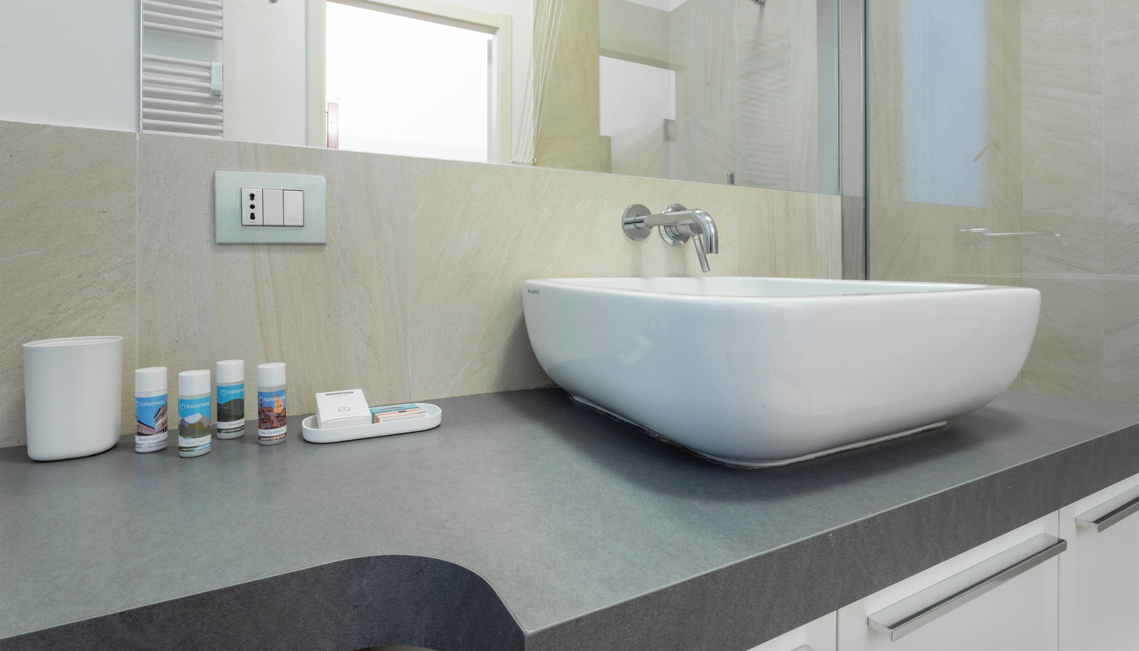 A bathroom with a large white sink, a mirror, and a countertop with toiletries.
