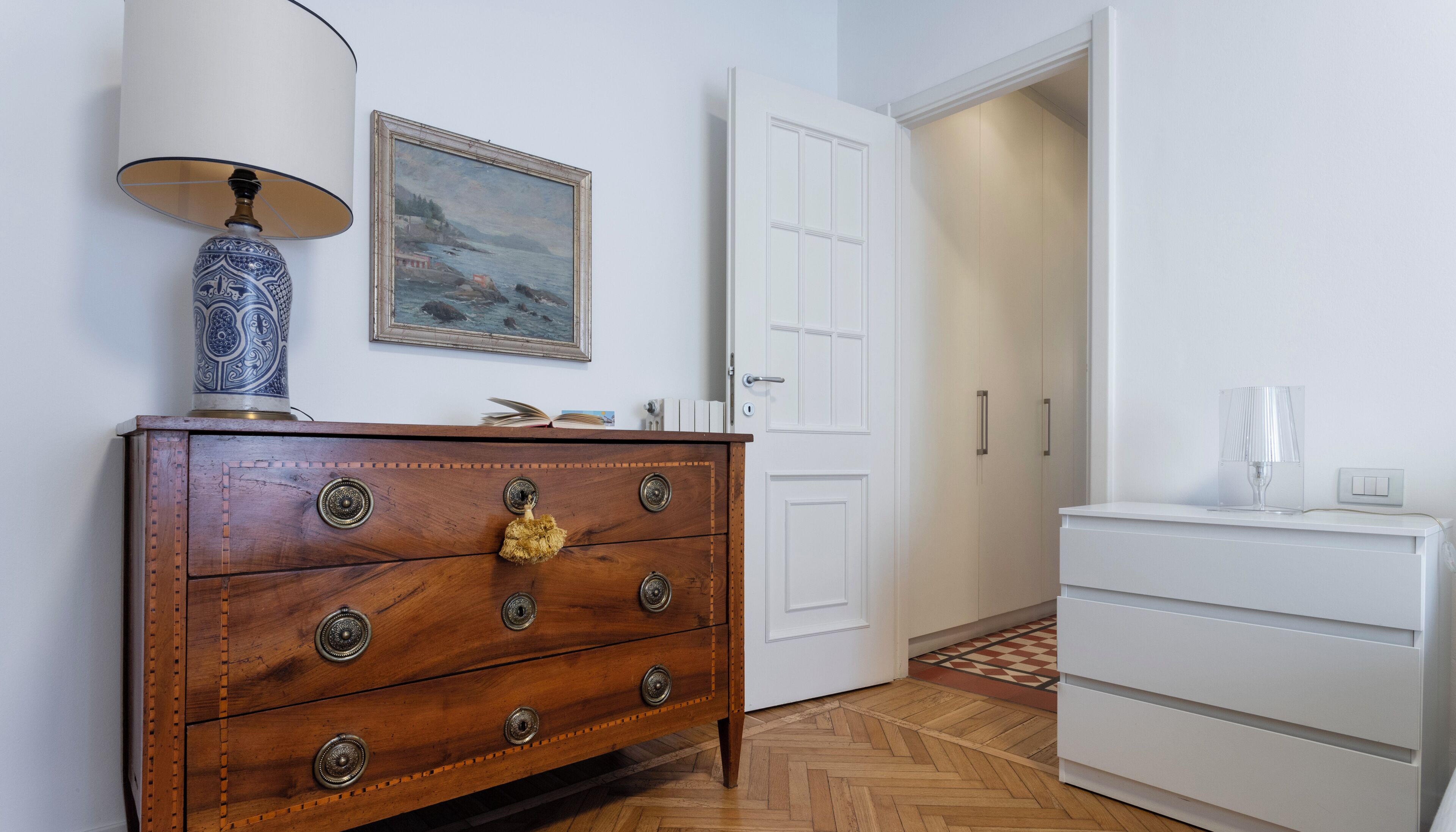A wooden dresser with ornate handles, a framed painting above it, and a white door in the background.