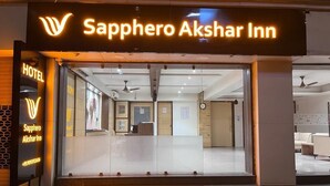 The entrance of Saphero Akshar Inn with a glass facade, a reception desk, and a visible interior with a ceiling fan.
