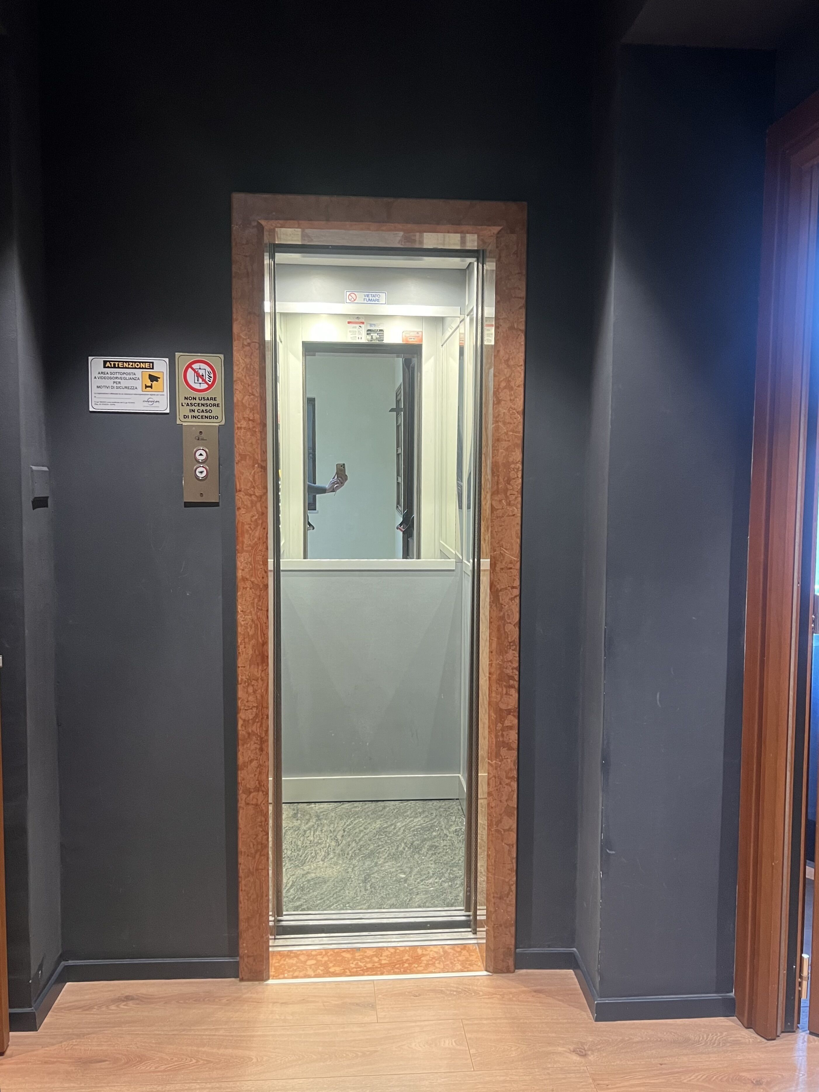 Un ascensore con struttura in legno, un cartello che vieta di fumare e un segnale di istruzioni per la sicurezza.