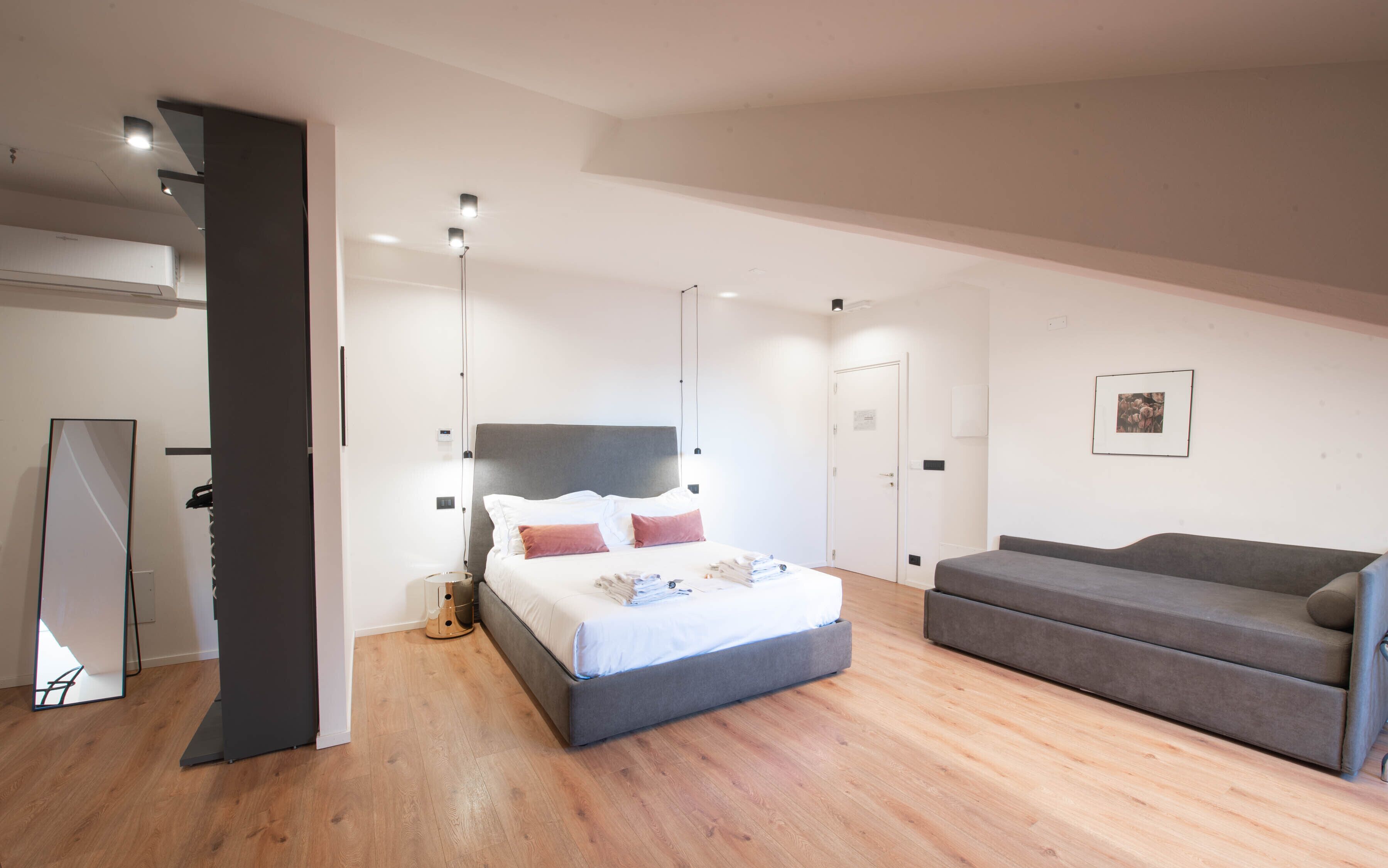 Un dormitorio moderno con cama, sofá, espejo y una puerta.