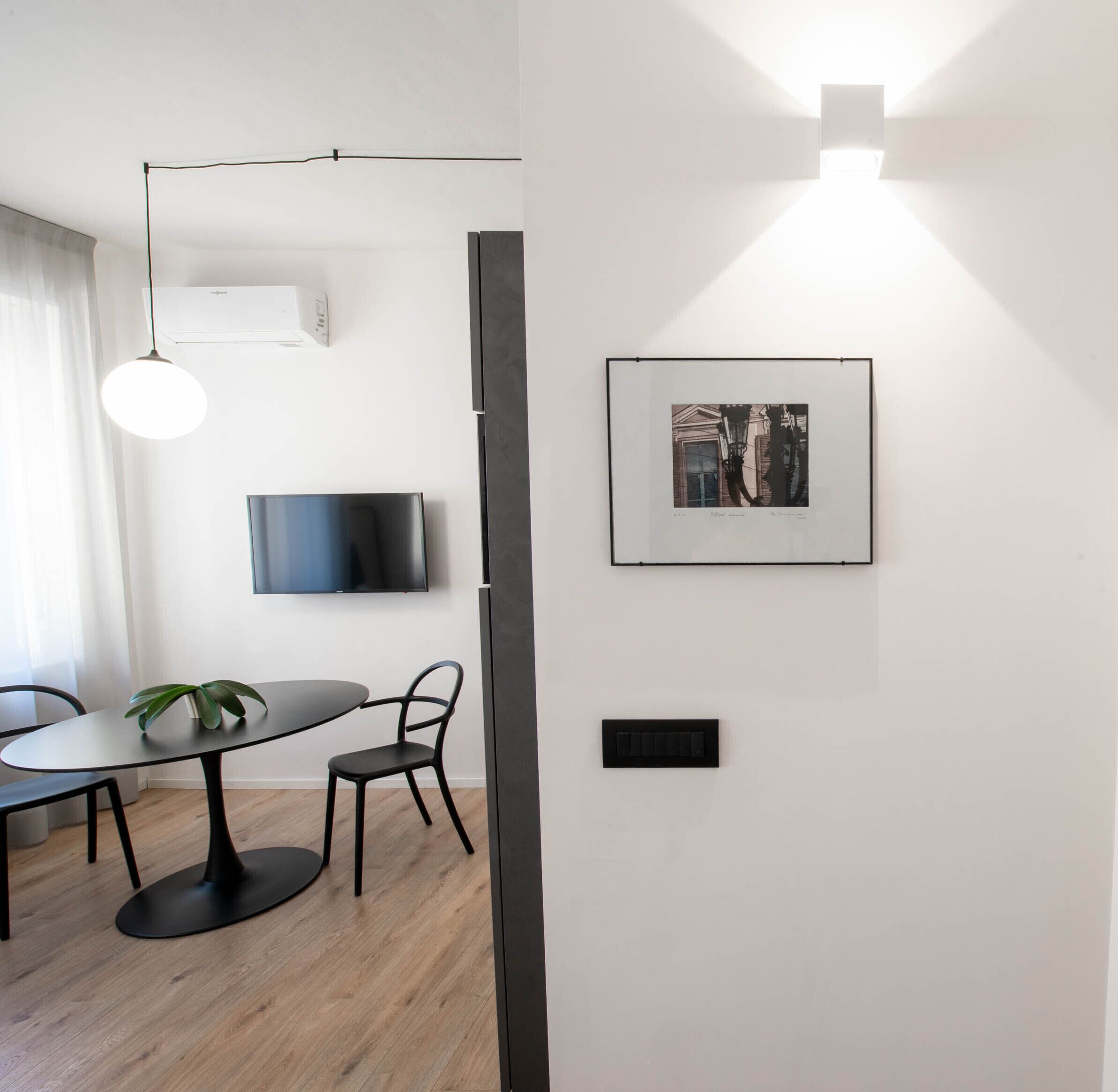 Ein modernes Wohnzimmer mit Essbereich, einem an der Wand befestigten Flachbildfernseher, einer Pendelleuchte und einem gerahmten Bild.
