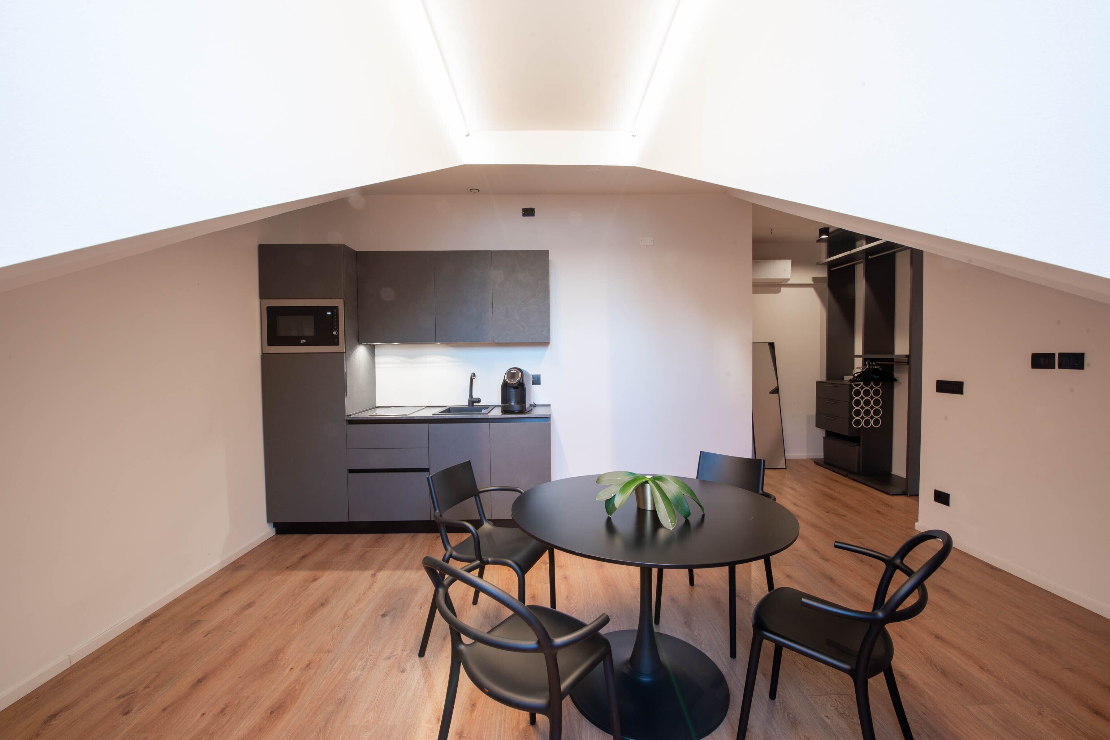 A compact kitchen with modern appliances, a dining area with a round table and chairs, and a skylight above.