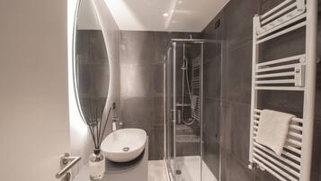 A modern bathroom with a glass-enclosed shower, a white sink, and a towel rack.