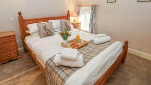 Un lit bien fait, recouvert d’une couverture à carreaux, deux oreillers ornés de motifs de lapins, un plateau avec des croissants et du jus d’orange, et une table de chevet avec une lampe et un miroir.