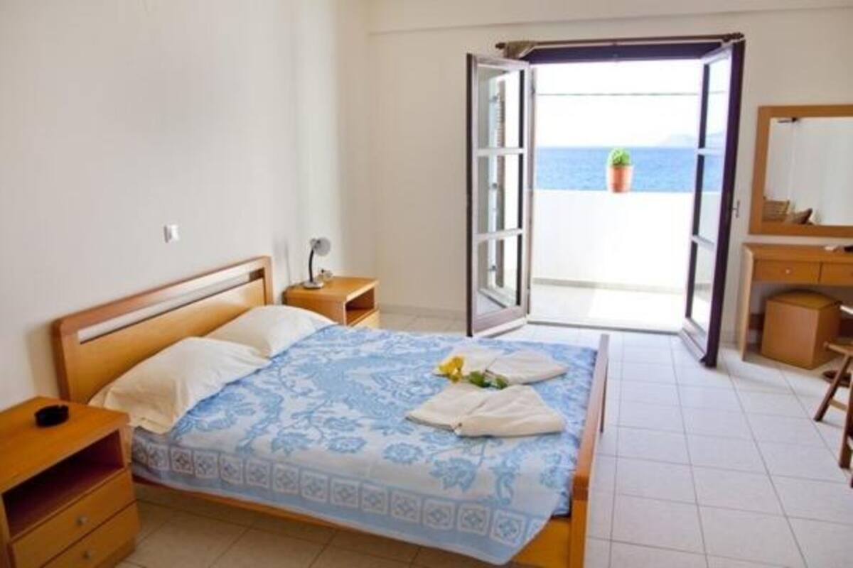 Un dormitorio con cama, mesita de noche, cómoda y puerta abierta que da a un balcón con vista al mar.