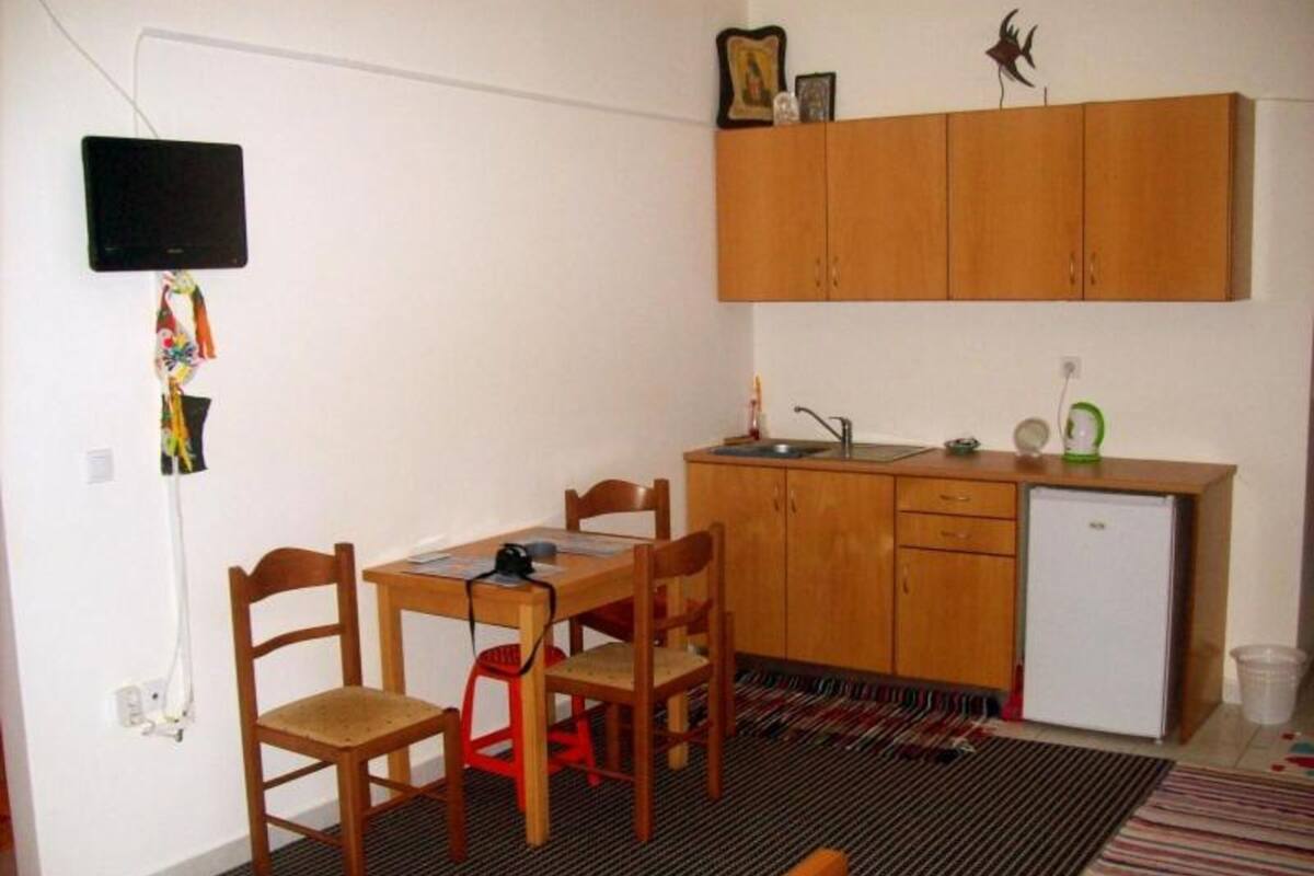 Una habitación compacta con una mesa de madera, dos sillas, una kitchenette pequeña, una cama y un televisor instalado en la pared.