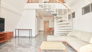A spacious living area with a high ceiling, a modern spiral staircase, a sofa, a coffee table, and a TV on a wooden cabinet.
