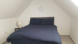 Een slaapkamer met een bed, nachtkastje, lamp en stopcontact.