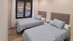 Habitación de hotel con dos camas, una ventana con cortinas, una lámpara en el techo y un aire acondicionado de pared.