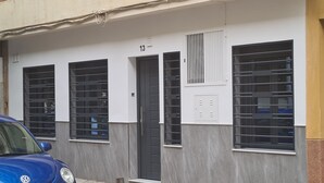 Un edificio con el número 13 sobre la puerta, un coche azul estacionado al frente y ventanas protegidas con rejas.