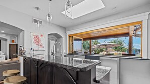 A modern kitchen with a large island, bar stools, and a view of the outdoors. - Location, Location!! Unforgettable Sunsets-Balloon Fiesta dream home! (Albuquerque)