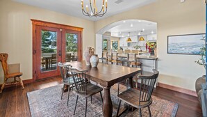 A dining area with a large wooden table, multiple chairs, and a chandelier. There is a view of the kitchen through an archway. - Location, Location!! Unforgettable Sunsets-Balloon Fiesta dream home! (Albuquerque)