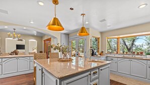 A spacious kitchen with a large island, pendant lighting, and a view of the outdoors through a large window. - Location, Location!! Unforgettable Sunsets-Balloon Fiesta dream home! (Albuquerque)