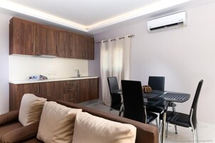 Una cucina compatta con mobili in legno, un tavolo da pranzo con sedie e un condizionatore d'aria.