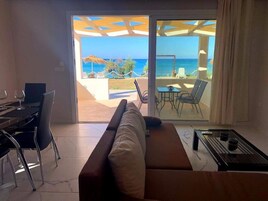 A room with a sofa, dining table, chairs, and a view of the ocean.