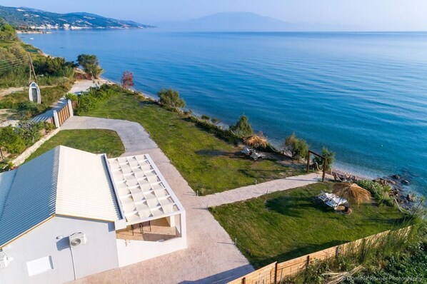 Una propiedad costera con un edificio blanco grande, un área verde y vista al mar.