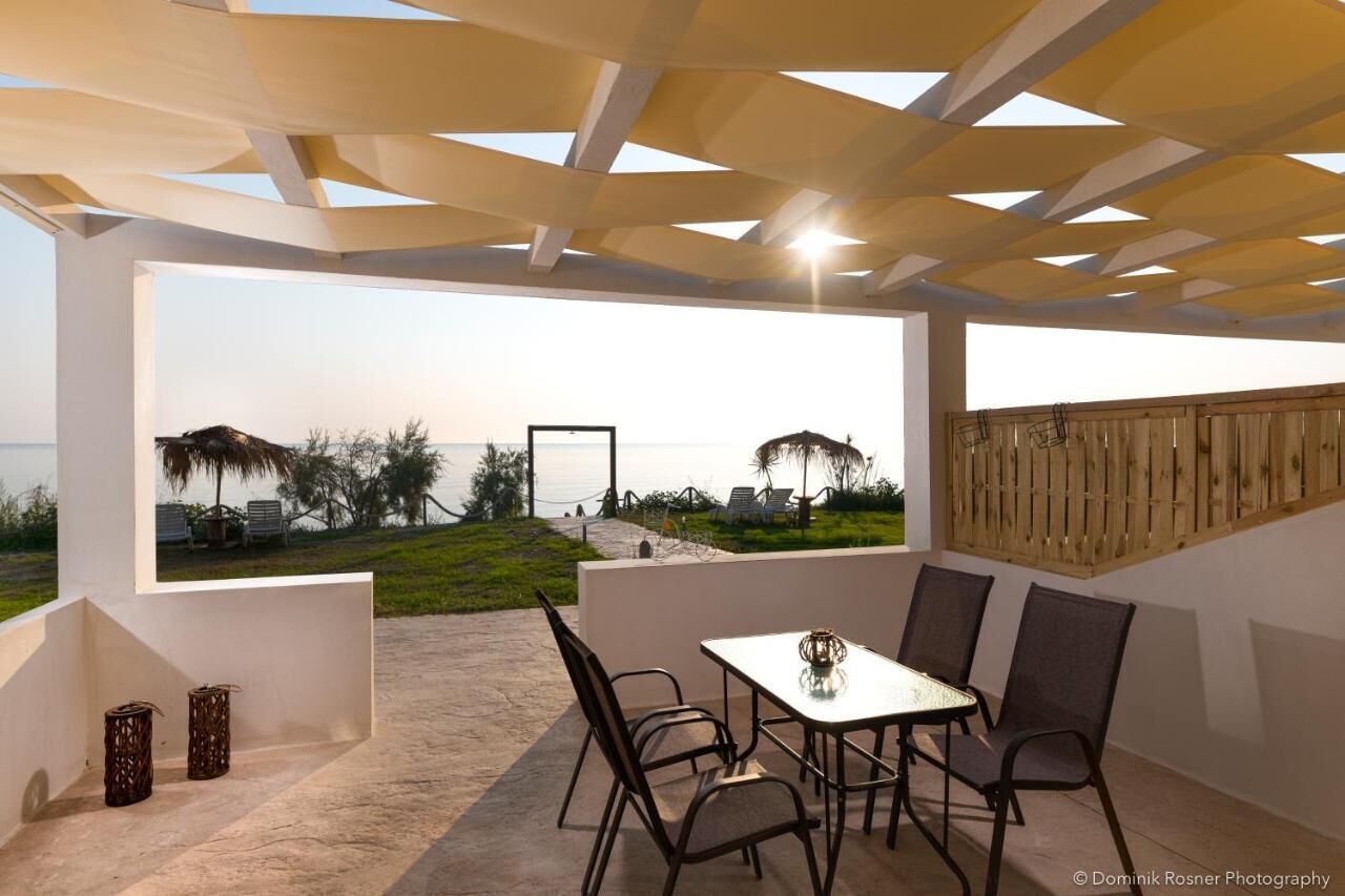 An outdoor patio with a table and chairs, overlooking a beach with umbrellas and chairs.