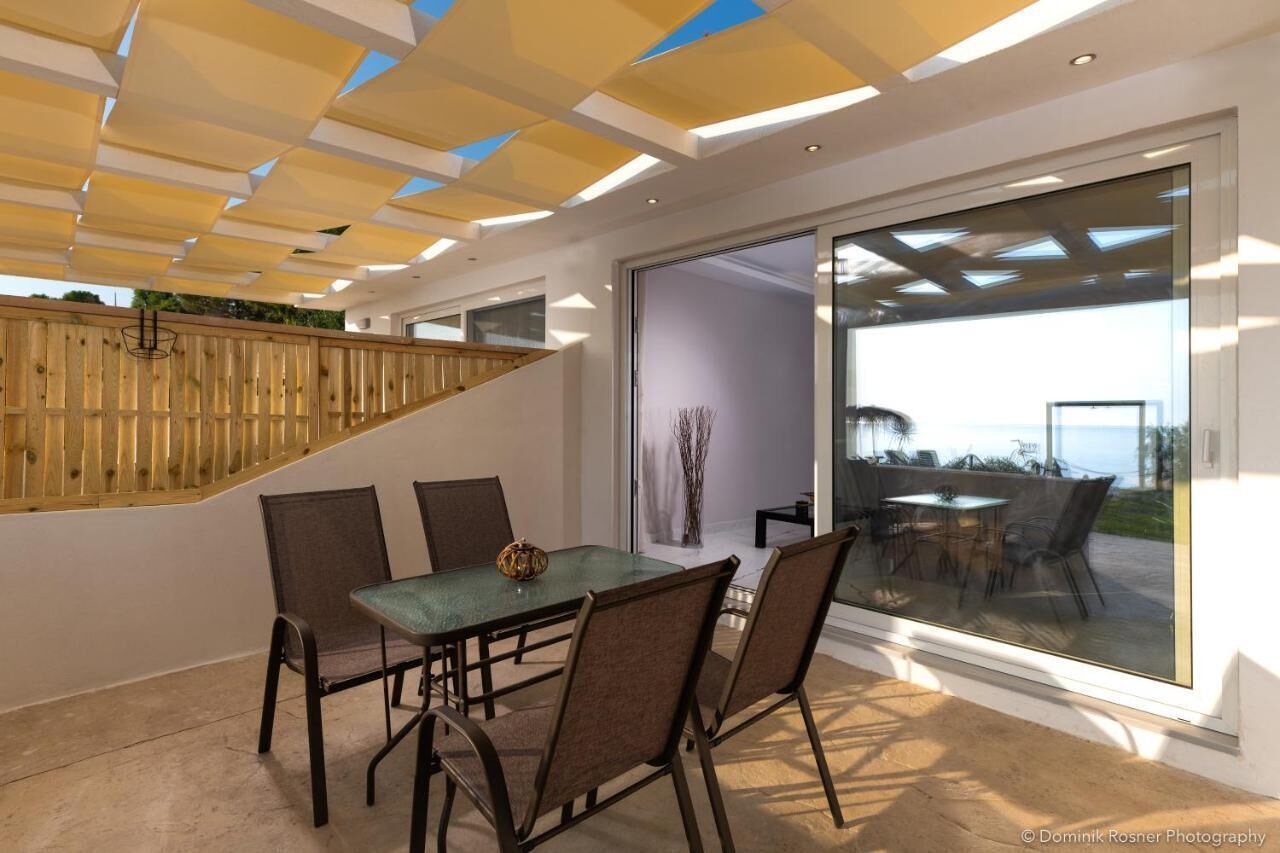 A modern dining area with a glass table and chairs, a wooden partition, and a view through large glass doors.