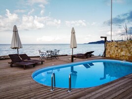 A wooden deck with a pool, lounge chairs, and umbrellas overlooking a body of water.