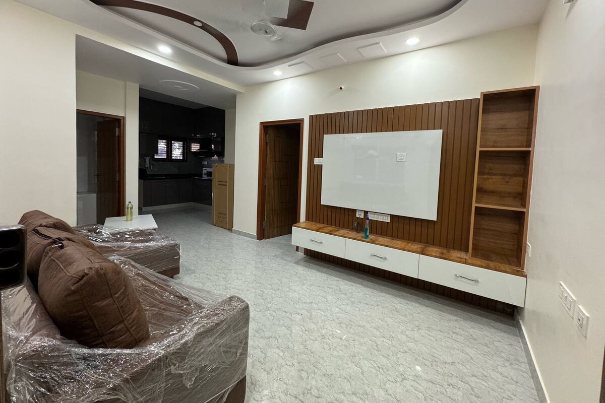 Una sala de estar moderna con un televisor grande, un panel de pared de madera y un sofá cubierto de plástico.
