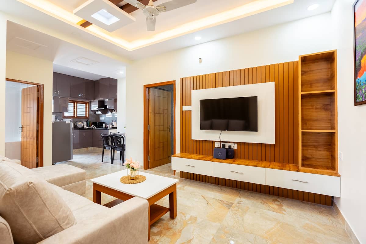 Una sala moderna con una televisión de pantalla plana, paneles de madera, un comedor y una cocina al fondo.
