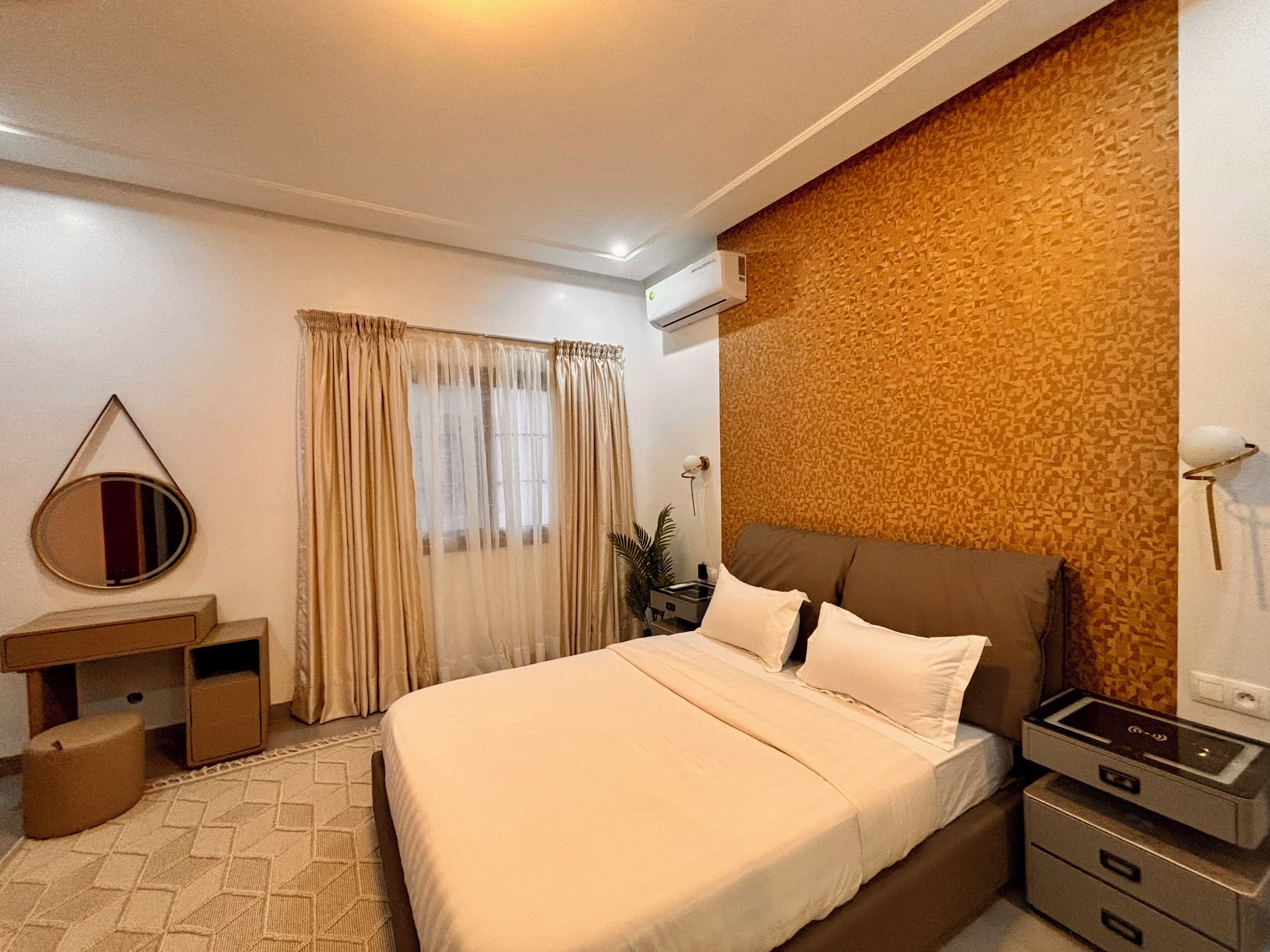 Habitación de hotel con cama, mesitas de noche, escritorio, espejo, unidad de aire acondicionado y pared con diseño.