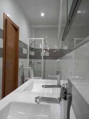 Casa de banho moderna com duas pias, chuveiro e sanita.