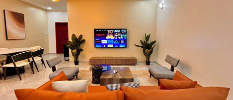 A modern living room with a sofa, chairs, a coffee table, and a flat-screen TV mounted on the wall.
