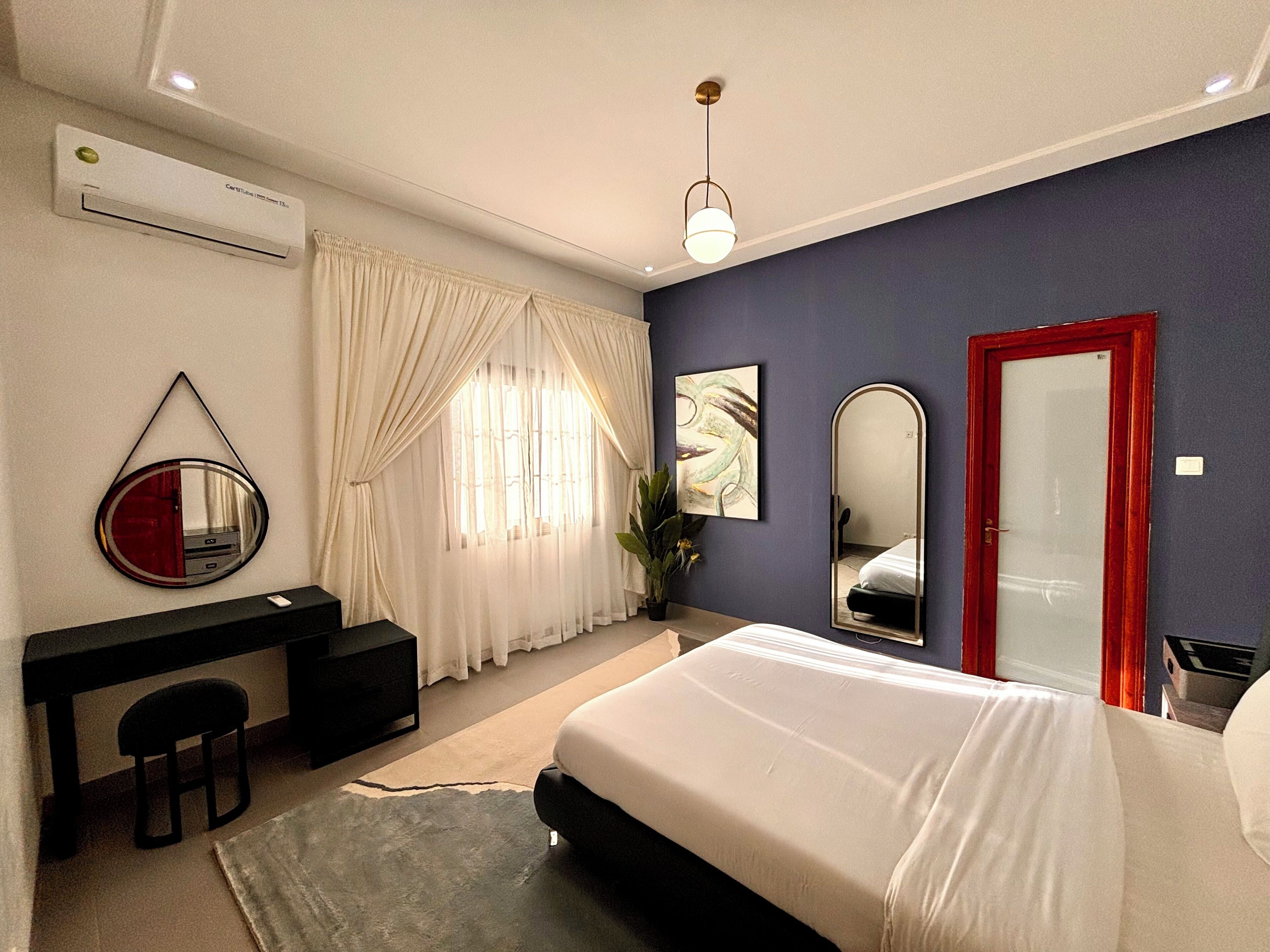 A bedroom with a bed, a desk, a chair, a mirror, and a door.