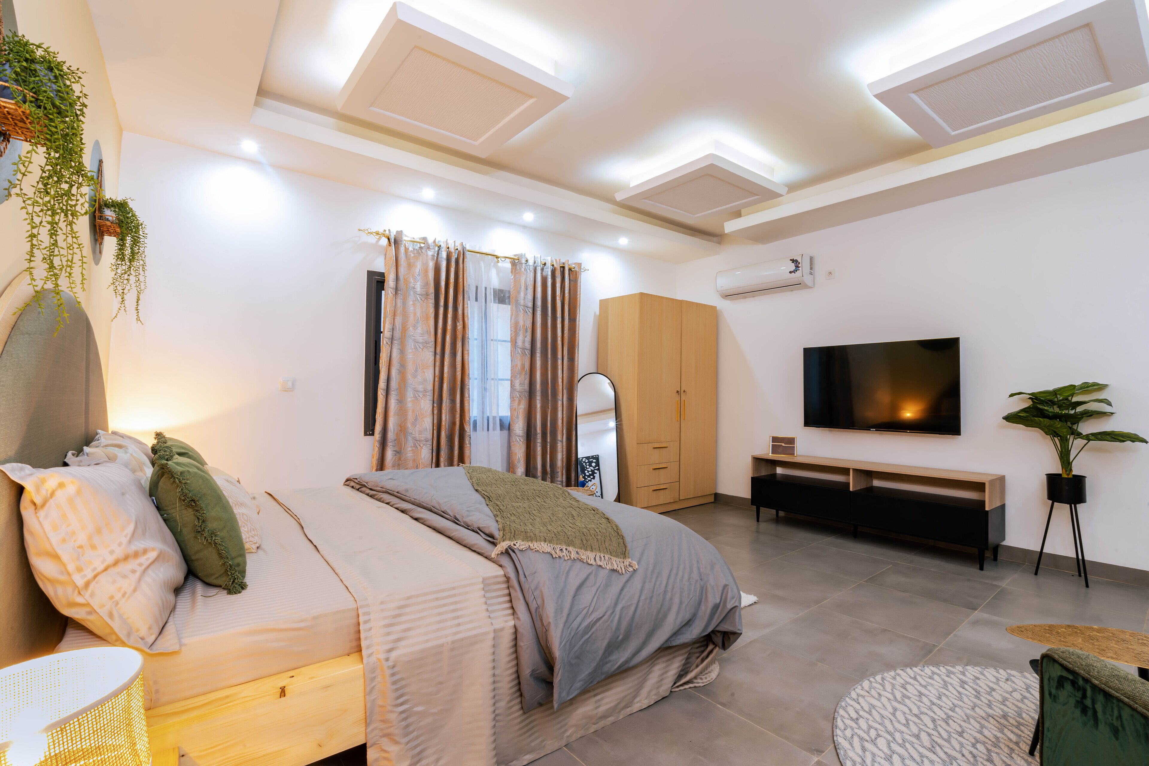 Un dormitorio moderno con cama, mesita de noche, televisor, armario y una planta en maceta.
