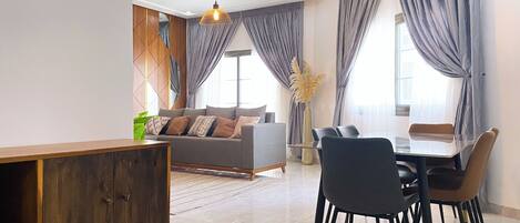 A modern living room with a sofa, dining table, and chairs. There is a wooden cabinet and a hanging light fixture.