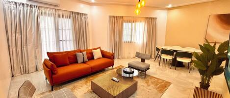 Una sala de estar con un sofá, sillones, una mesa de centro, una mesa de comedor con sillas y una planta en maceta.