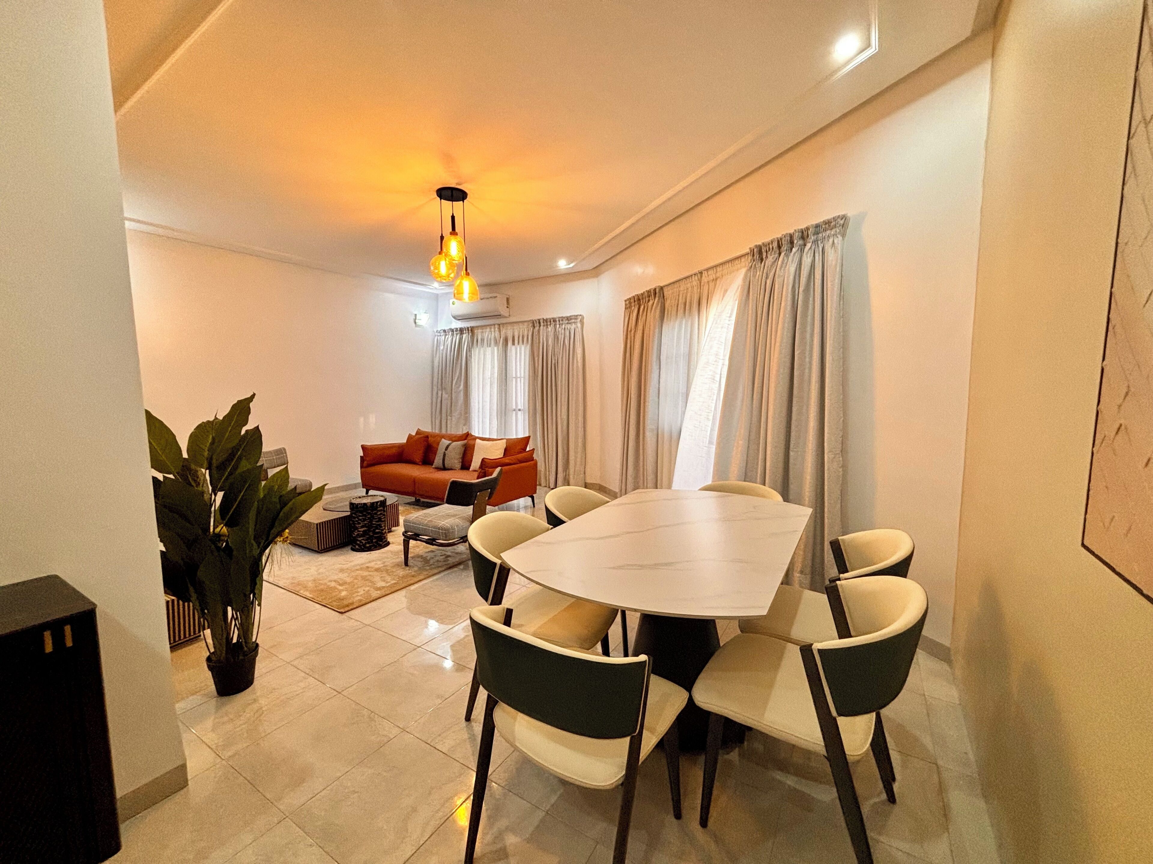 A modern living room with a dining area, featuring a sofa, a table, and chairs.