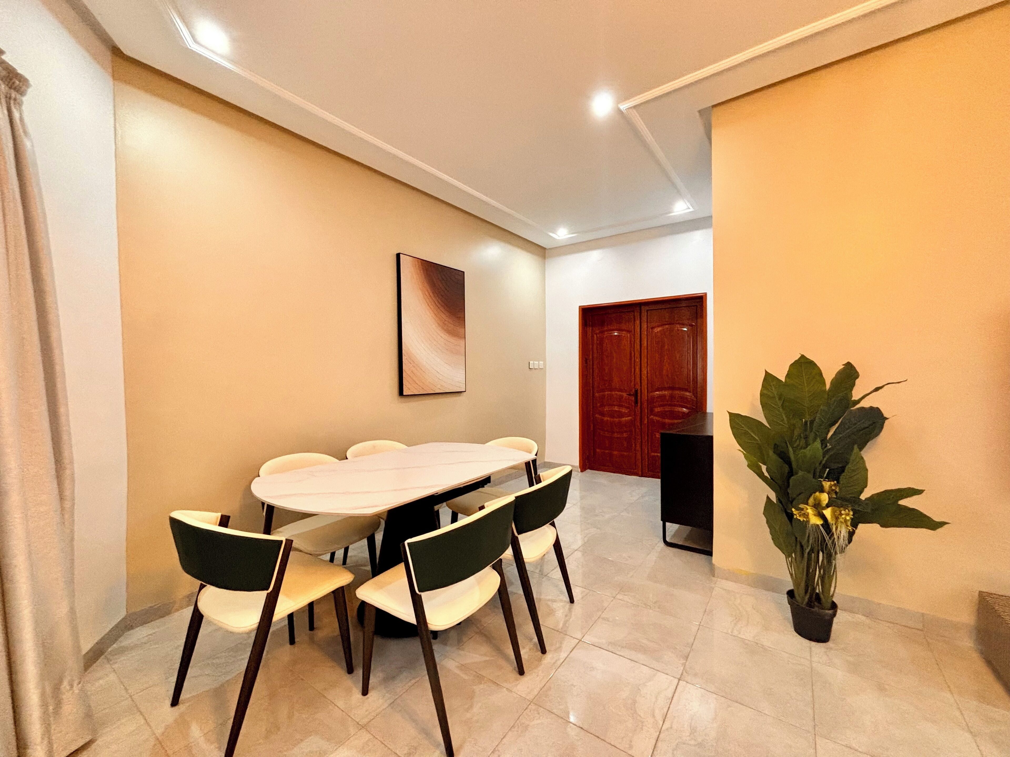 A conference room with a long table, several chairs, a potted plant, and a wooden door in the background.