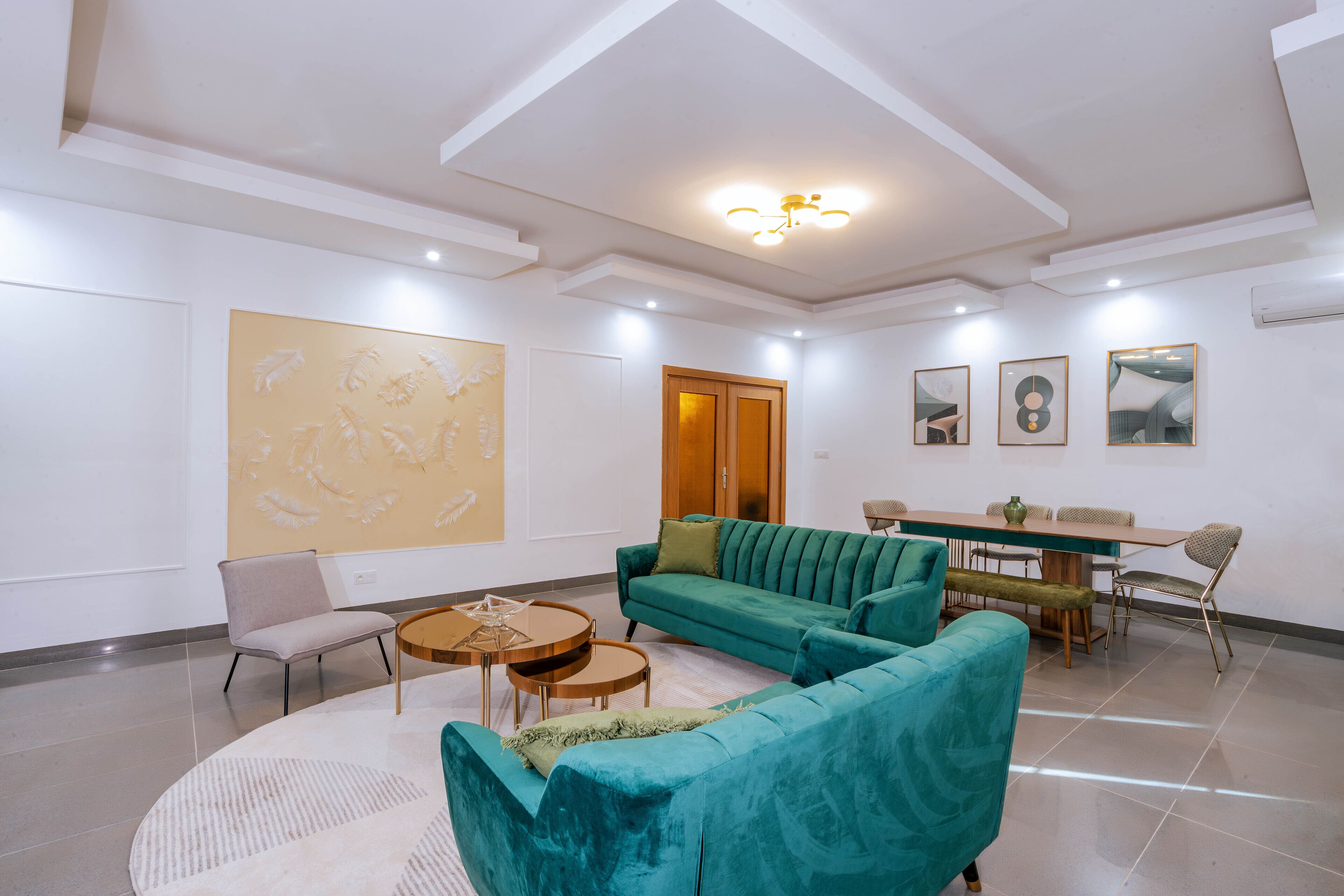 A modern living room with a teal sofa, a round coffee table, and a dining area with a wooden table and chairs.
