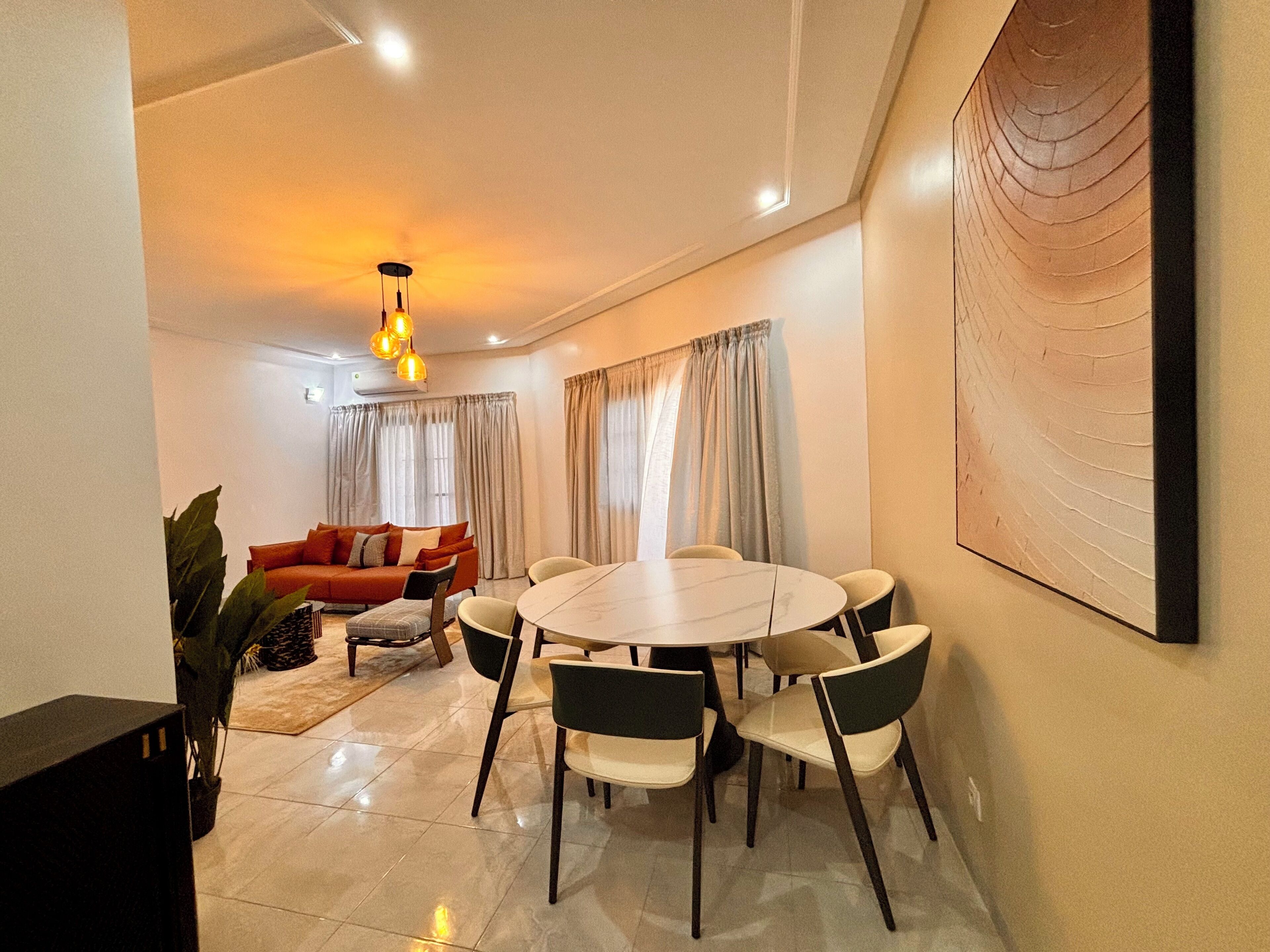 A modern living room with a round dining table, a sofa, and a large abstract painting on the wall.