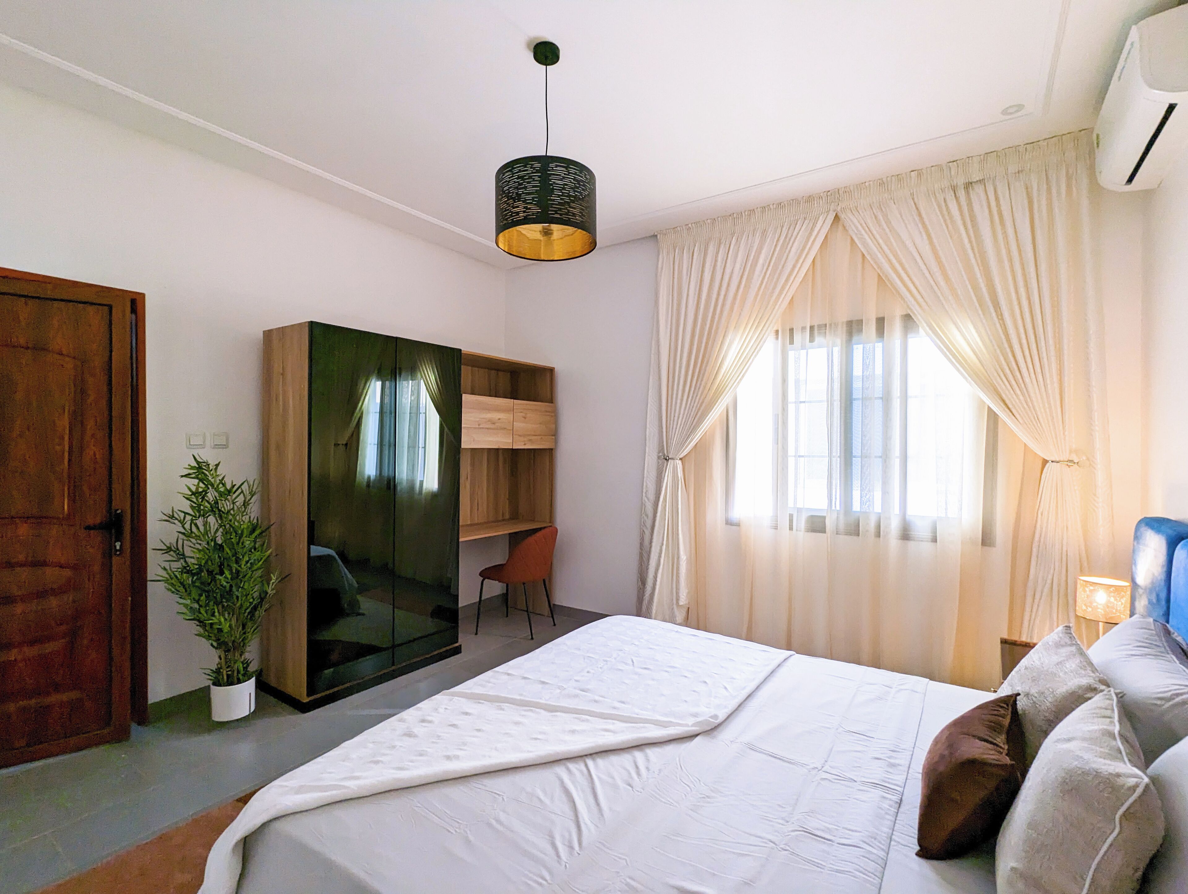 Une chambre à coucher avec un lit, un bureau et une chaise. On y trouve également une plante et une armoire.